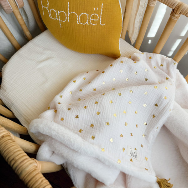 La couverture est une des pièces indispensable du trousseau de bébé. Parfaite en cadeau de naissance ou à s’offrir soit même, cette couverture chaude spéciale “bébés d’hiver”, vous accompagnera très longtemps dans vos moments câlins avec bébé. Les bébés d’hiver qui naissent pendant les mois les plus froids ont besoin d'être tenus bien au chaud à la sortie du ventre de maman. C'est pourquoi nous avons conçu cette couverture chaude spéciale “bébé d’hiver”. Dès son arrivée, bébé passe d'un environnement clos de 37°C à une température extérieure souvent très basse en hiver. C'est pour cela que nos couvertures d'hiver épaisses sont idéales pour réguler et maintenir une bonne température pour le corps de bébé. Comme toutes nos couvertures elle est très souple et enveloppera parfaitement bébé. Cette grande couverture pourra également être utilisée en descente de lit quand bébé sera plus grand. Cette couverture est idéale pour bien réchauffer les bébés d’hiver grâce à sa fausse fourrure extra douce grège, très épaisse (365g/m2), et sa doublure en gaze de coton hypoallergénique au joli petit motif trèfles dorés, un motif plein de sens parfois pour certaines histoires ...  Quatre pompons en laine  dorée viennent sublimer la couverture dans les angles. Ils sont fabriqués à la main pour une pièce encore plus unique. Chaque pompon est posé très fermement avec des points solides afin de garantir une sécurité optimale pour votre enfant.