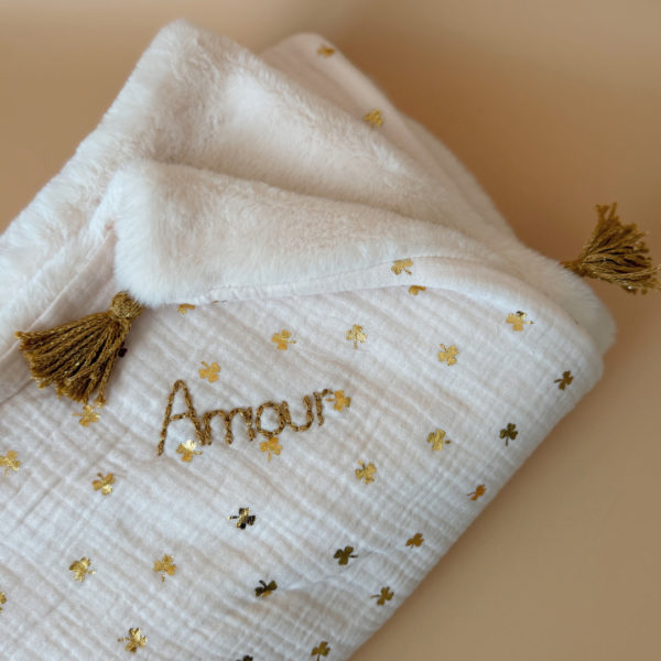 La couverture est une des pièces indispensable du trousseau de bébé. Parfaite en cadeau de naissance ou à s’offrir soit même, cette couverture chaude spéciale “bébés d’hiver”, vous accompagnera très longtemps dans vos moments câlins avec bébé. Les bébés d’hiver qui naissent pendant les mois les plus froids ont besoin d'être tenus bien au chaud à la sortie du ventre de maman. C'est pourquoi nous avons conçu cette couverture chaude spéciale “bébé d’hiver”. Dès son arrivée, bébé passe d'un environnement clos de 37°C à une température extérieure souvent très basse en hiver. C'est pour cela que nos couvertures d'hiver épaisses sont idéales pour réguler et maintenir une bonne température pour le corps de bébé. Comme toutes nos couvertures elle est très souple et enveloppera parfaitement bébé. Cette grande couverture pourra également être utilisée en descente de lit quand bébé sera plus grand. Cette couverture est idéale pour bien réchauffer les bébés d’hiver grâce à sa fausse fourrure extra douce grège, très épaisse (365g/m2), et sa doublure en gaze de coton hypoallergénique au joli petit motif trèfles dorés, un motif plein de sens parfois pour certaines histoires ...  Quatre pompons en laine  dorée viennent sublimer la couverture dans les angles. Ils sont fabriqués à la main pour une pièce encore plus unique. Chaque pompon est posé très fermement avec des points solides afin de garantir une sécurité optimale pour votre enfant.