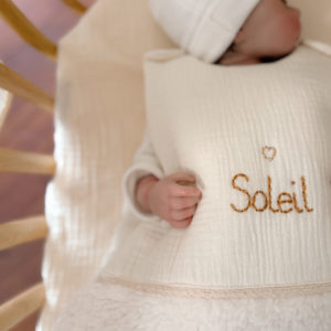 Cette gigoteuse pour bébé, confectionnée avec soin, est le choix idéal pour garder bébé au chaud durant l’hiver. Fabriquée en fausse fourrure type sherpa et en gaze de coton écrue, elle allie douceur et élégance. Son design raffiné, avec un empiècement en gaze de coton orné d'un discret galon en coton ajouré, en fait un accessoire de choix pour un sommeil cosy et stylé. Personnalisez la gigoteuse de bébé Vous avez la possibilité de personnaliser la gigoteuse avec le prénom ou le surnom de bébé, brodé à la main de la couleur de votre choix. La broderie est effectuée sur le milieu devant de la gigoteuse. Cette gigoteuse est parfaite pour : Garantir un sommeil chaud et confortable lors des nuits fraîches de l'hiver. Apporter une touche de raffinement à la chambre de bébé grâce à son design élégant. Offrir un cadeau de naissance pratique et raffiné. Avantages : Équivalent TOG 3 pour des chambres entre 18°C et 22°C Chaleur et confort : La fausse fourrure sherpa combinée à la doublure ouatinée apporte un confort thermique maximal. Élégance intemporelle : La broderie anglaise et l’empiècement en gaze de coton ajoutent un détail chic à cette gigoteuse. Pratique : Facile à enfiler et sécurisée, elle garantit un sommeil paisible sans risque de déperdition de chaleur.