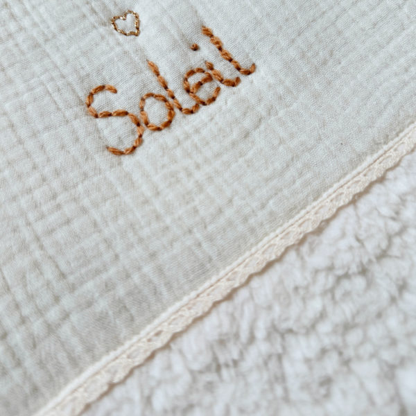 Cette gigoteuse pour bébé, confectionnée avec soin, est le choix idéal pour garder bébé au chaud durant l’hiver. Fabriquée en fausse fourrure type sherpa et en gaze de coton écrue, elle allie douceur et élégance. Son design raffiné, avec un empiècement en gaze de coton orné d'un discret galon en coton ajouré, en fait un accessoire de choix pour un sommeil cosy et stylé. Personnalisez la gigoteuse de bébé Vous avez la possibilité de personnaliser la gigoteuse avec le prénom ou le surnom de bébé, brodé à la main de la couleur de votre choix. La broderie est effectuée sur le milieu devant de la gigoteuse. Cette gigoteuse est parfaite pour : Garantir un sommeil chaud et confortable lors des nuits fraîches de l'hiver. Apporter une touche de raffinement à la chambre de bébé grâce à son design élégant. Offrir un cadeau de naissance pratique et raffiné. Avantages : Équivalent TOG 3 pour des chambres entre 18°C et 22°C Chaleur et confort : La fausse fourrure sherpa combinée à la doublure ouatinée apporte un confort thermique maximal. Élégance intemporelle : La broderie anglaise et l’empiècement en gaze de coton ajoutent un détail chic à cette gigoteuse. Pratique : Facile à enfiler et sécurisée, elle garantit un sommeil paisible sans risque de déperdition de chaleur.