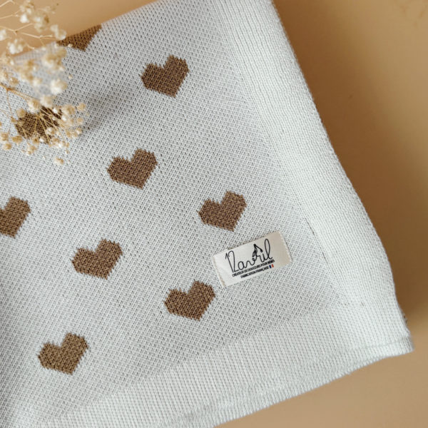 La couverture de naissance 12avril est bien plus qu’un simple accessoire : c’est un cocon de douceur et de chaleur, imaginé et tricoté avec soin en France, au cœur de la région roannaise, réputée pour son savoir-faire textile. Avec son motif all-over de petits cœurs biscuit délicatement posés sur un fond écru, elle séduit au premier regard par son esthétique tendre et intemporelle. Cette couverture est pensée pour réchauffer bébé tout en apportant une touche élégante et raffinée à sa chambre ou à vos sorties. Conçue à partir d’un fil de qualité, composé à 50% de laine, elle offre la chaleur idéale pour l’hiver tout en restant respirante. Sa texture tricotée apporte un confort douillet et une grande souplesse, parfaite pour envelopper bébé lors des siestes, des promenades ou des moments de tendresse à la maison. De forme carrée (80 x 80 cm), elle est parfaitement adaptée aux tout-petits : facile à plier, à transporter et à utiliser dans un berceau, une poussette ou un siège-auto. Elle accompagnera bébé partout, dès la naissance, en offrant une sensation rassurante de cocon et de sécurité. Chaque couverture est le fruit d’une confection locale, valorisant le savoir-faire français et une production respectueuse. C’est un cadeau de naissance idéal, qui allie esthétisme, praticité et authenticité. Offrir ou s’offrir la couverture de naissance 12avril, c’est choisir un produit de caractère, plein de tendresse, pensé pour durer et transmettre la chaleur de l’amour dès les premiers jours de vie.