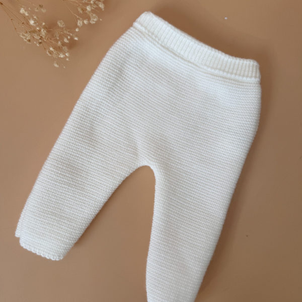 Offrez à votre bébé un premier vêtement doux, élégant et entièrement fabriqué en France avec cet adorable ensemble de naissance en maille blanche. Composé d'une brassière au col en dentelle de coton et d'un pantalon assorti, cet ensemble est tricoté avec soin dans une maille jersey, un point traditionnel qui lui confère un relief raffiné et un toucher délicatement texturé. La brassière croisée s'attache facilement grâce à de petits boutons  pour habiller bébé tout en douceur et sans effort. Le pantalon à taille élastiquée  assure un confort optimal et un bon maintien, sans comprimer le ventre fragile des nouveau-nés. Ce modèle est intégralement tricoté en France, en collaboration avec un atelier partenaire reconnu pour son savoir-faire en maille fine pour bébé. Une attention toute particulière est portée à la qualité des finitions, pour un rendu chic, intemporel et parfaitement adapté à la peau des tout-petits. Et pour rendre ce cadeau de naissance encore plus unique, vous pouvez choisir de personnaliser la brassière avec une broderie faite main, directement au centre du vêtement. Que ce soit le prénom du bébé ou un petit mot doux, chaque pièce devient ainsi un souvenir précieux, plein d’émotion.
