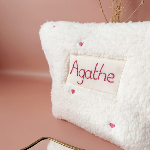 La conception de la trousse permet aux produits de bébé de tenir debout à l'intérieur, ce qui facilite l'organisation et l'accès aux produits essentiels. Liniment, couches, lait de toilette, cotons, autant de produits pour un si petit bout de chou, que vous aurez besoin d'une grande trousse de toilette spacieuse. Fabriquée en fausse fourrure sherpa écrue, elle est joliment brodée avec de petits coeurs rose. Cette trousse est à la fois douce et durable. L'intérieur de la trousse est doublé avec un tissu imperméable. Ls liquides renversés ne pénètrent pas à l'extérieur, protégeant ainsi les autres articles dans le sac à langer. Personnaliser votre trousse de toilette, au doux prénom de bébé ! La personnalisation est réalisée à la main sur le devant de la trousse de toilette avec un fil du coloris de votre choix.  C'est un plaston qui agrémente le devant de la trousse avec le prénom de bébé. Fièrement fabriquée en France, cette trousse de toilette est le fruit d'un savoir-faire artisanal et d'une attention particulière aux détails. Zoom sur le petit curseur de la fermeture à glissière ! Découvrez notre gamme entière de produits autour du bain : de belles et grandes capes de bain XXL, langes et débarbouillettes. 