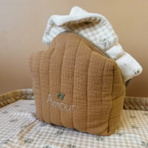 La trousse de toilette pour bébé est une pièce personnalisée et pratique, conçue avec soin pour répondre aux besoins des parents et de leur nouveau-né. Vous serez conquis par son grand format. La conception de la trousse permet aux produits de bébé de tenir debout à l'intérieur, ce qui facilite l'organisation et l'accès aux produits essentiels. Liniment, couches, lait de toilette, cotons, autant de produits pour un si petit bout de chou, que vous aurez besoin d'une grande trousse de toilette spacieuse. Fabriquée en gaze de coton matelassée, cette trousse est à la fois douce et durable. L'intérieur de la trousse est doublé avec un tissu imperméable. Les liquides renversés ne pénètrent pas à l'extérieur, protégeant ainsi les autres articles dans le sac. Personnaliser votre trousse de toilette, au doux prénom de bébé ! La personnalisation est réalisée à la main sur le devant de la trousse de toilette. Fièrement fabriquée en France, cette trousse de toilette est le fruit d'un savoir-faire artisanal et d'une attention particulière aux détails. Zoom sur le petit curseur de la fermeture à glissière ! Découvrez notre gamme entière de produits de ce thème: langes, couvertures, doudous lange...