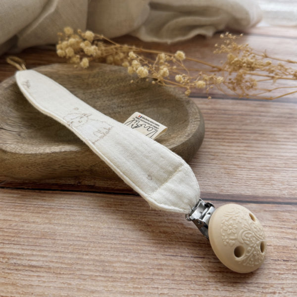 Élégante, douce et sécurisée, notre attache tétine en gaze de coton  accompagne bébé au quotidien tout en ajoutant une touche délicate à sa tenue. Chaque modèle est personnalisable avec le prénom de bébé, soigneusement brodé à la main, pour créer un accessoire unique et plein de sens. Dotée d’un lien doré raffiné pour fixer la tétine et d’une pince ronde en silicone embossé, elle allie esthétique et praticité.