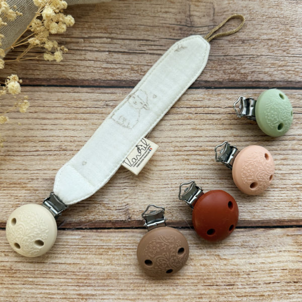 Élégante, douce et sécurisée, notre attache tétine en gaze de coton  accompagne bébé au quotidien tout en ajoutant une touche délicate à sa tenue. Chaque modèle est personnalisable avec le prénom de bébé, soigneusement brodé à la main, pour créer un accessoire unique et plein de sens. Dotée d’un lien doré raffiné pour fixer la tétine et d’une pince ronde en silicone embossé, elle allie esthétique et praticité.