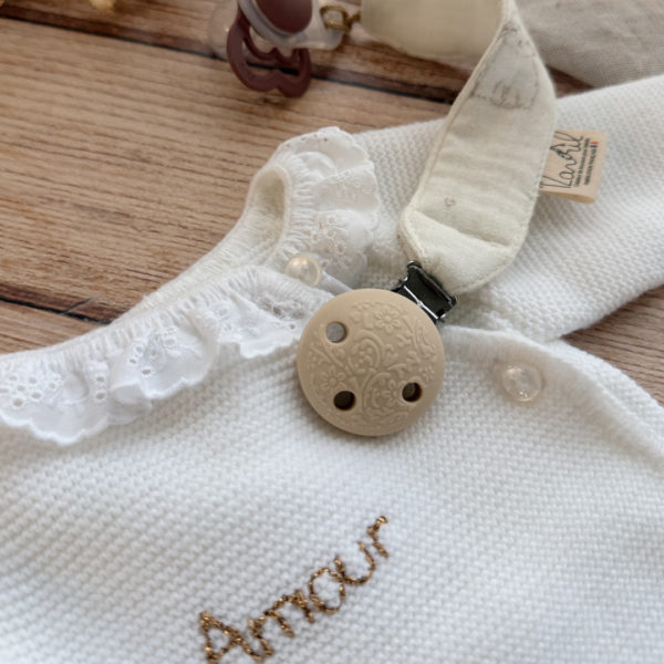 Élégante, douce et sécurisée, notre attache tétine en gaze de coton  accompagne bébé au quotidien tout en ajoutant une touche délicate à sa tenue. Chaque modèle est personnalisable avec le prénom de bébé, soigneusement brodé à la main, pour créer un accessoire unique et plein de sens. Dotée d’un lien doré raffiné pour fixer la tétine et d’une pince ronde en silicone embossé, elle allie esthétique et praticité.