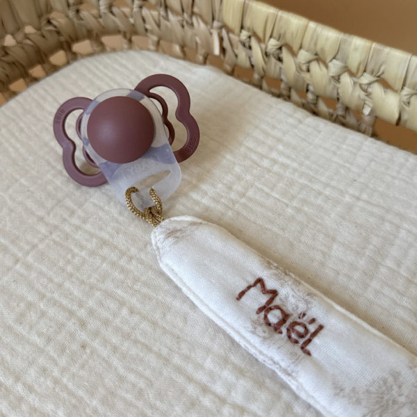 Élégante, douce et sécurisée, notre attache tétine en gaze de coton écrue accompagne bébé au quotidien tout en ajoutant une touche délicate à sa tenue. Chaque modèle est personnalisable avec le prénom de bébé, soigneusement brodé à la main, pour créer un accessoire unique et plein de sens. Dotée d’un lien doré raffiné pour fixer la tétine et d’une pince ronde en silicone embossé, elle allie esthétique et praticité.