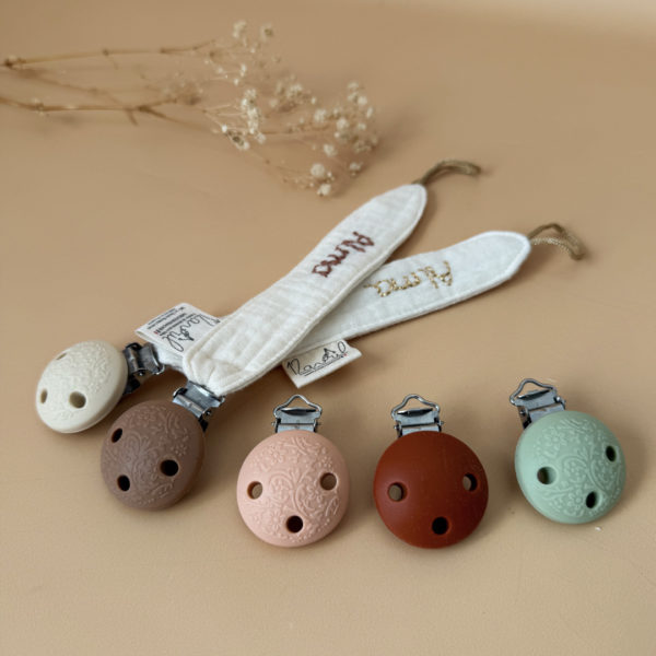 Élégante, douce et sécurisée, notre attache tétine en gaze de coton écrue accompagne bébé au quotidien tout en ajoutant une touche délicate à sa tenue. Chaque modèle est personnalisable avec le prénom de bébé, soigneusement brodé à la main, pour créer un accessoire unique et plein de sens. Dotée d’un lien doré raffiné pour fixer la tétine et d’une pince ronde en silicone embossé, elle allie esthétique et praticité.