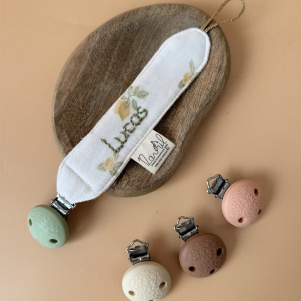 Élégante, douce et sécurisée, notre attache tétine en gaze de coton  accompagne bébé au quotidien tout en ajoutant une touche délicate à sa tenue. Chaque modèle est personnalisable avec le prénom de bébé, soigneusement brodé à la main, pour créer un accessoire unique et plein de sens. Dotée d’un lien doré raffiné pour fixer la tétine et d’une pince ronde en silicone embossé, elle allie esthétique et praticité.