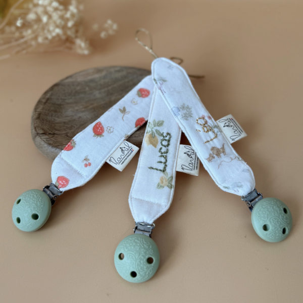 Élégante, douce et sécurisée, notre attache tétine en gaze de coton  accompagne bébé au quotidien tout en ajoutant une touche délicate à sa tenue. Chaque modèle est personnalisable avec le prénom de bébé, soigneusement brodé à la main, pour créer un accessoire unique et plein de sens. Dotée d’un lien doré raffiné pour fixer la tétine et d’une pince ronde en silicone embossé, elle allie esthétique et praticité.
