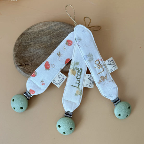 Élégante, douce et sécurisée, notre attache tétine en gaze de coton  accompagne bébé au quotidien tout en ajoutant une touche délicate à sa tenue. Chaque modèle est personnalisable avec le prénom de bébé, soigneusement brodé à la main, pour créer un accessoire unique et plein de sens. Dotée d’un lien doré raffiné pour fixer la tétine et d’une pince ronde en silicone embossé, elle allie esthétique et praticité.