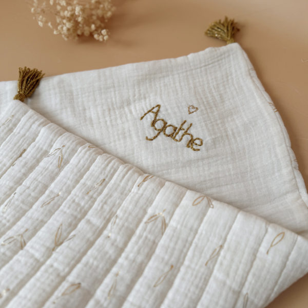 Découvrez la couverture idéale pour accompagner votre bébé pendant les beaux jours. Confectionnée en gaze de coton écrue et en gaze de coton matelassée aux délicats motifs feuillage doré, cette couverture allie douceur, légèreté et élégance.