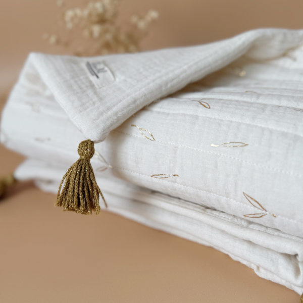 Découvrez la couverture idéale pour accompagner votre bébé pendant les beaux jours. Confectionnée en gaze de coton écrue et en gaze de coton matelassée aux délicats motifs feuillage doré, cette couverture allie douceur, légèreté et élégance.