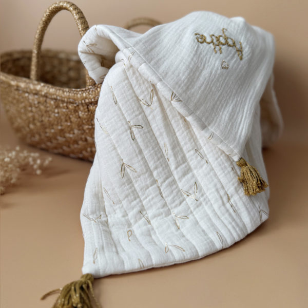 Découvrez la couverture idéale pour accompagner votre bébé pendant les beaux jours. Confectionnée en gaze de coton écrue et en gaze de coton matelassée aux délicats motifs feuillage doré, cette couverture allie douceur, légèreté et élégance.